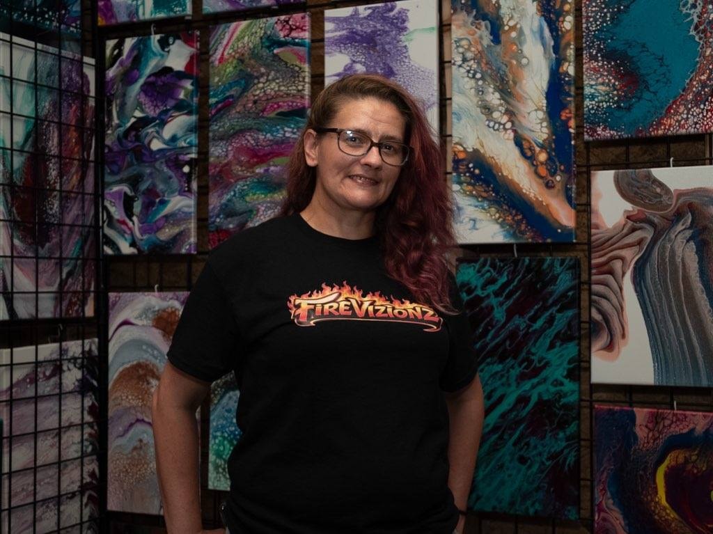 Fire Vizionz artist in her Fire Vizionz shirt surrounded by her paintings